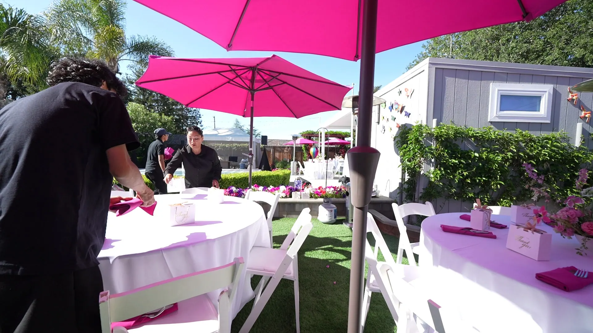 Round tables with pink umbrellas set on a Lafayette backyard lawn
