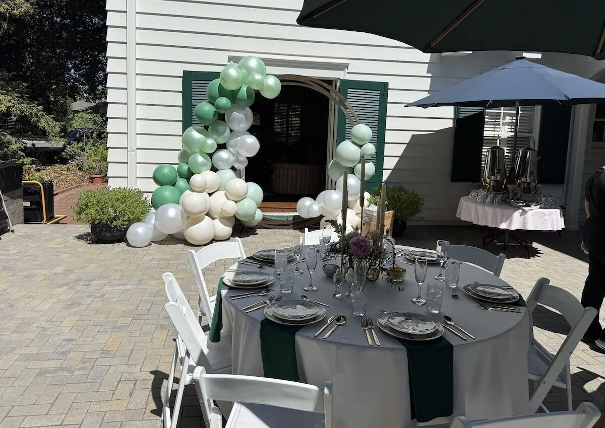 Sage and ivory balloon garland over a doorway paired with a bloom-accented tablescape — balloon and floral styling for Oakley catering parties