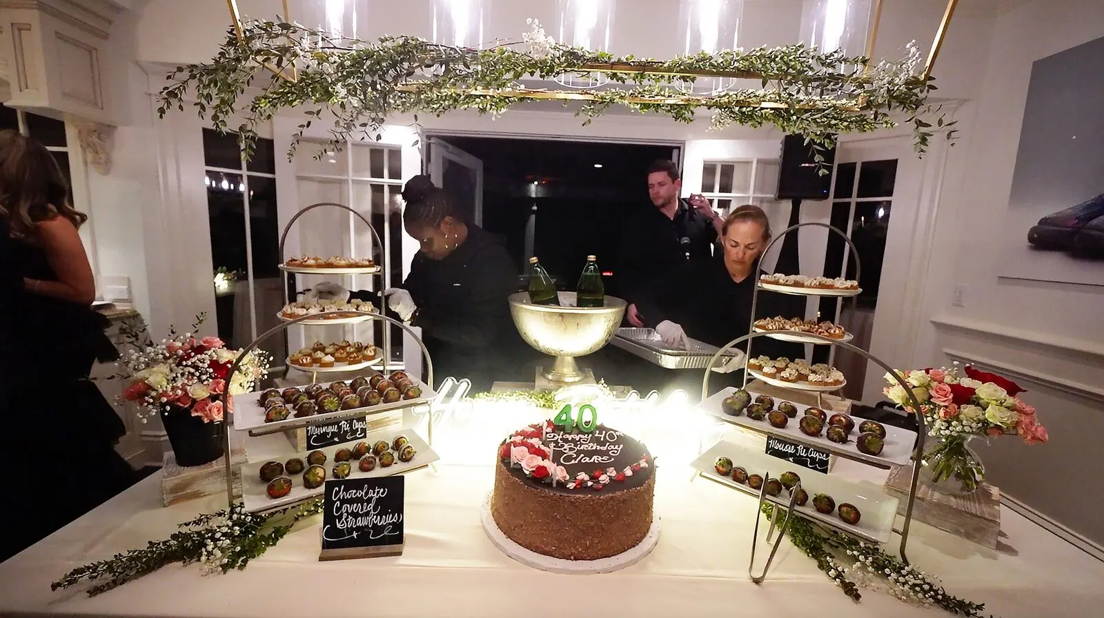 Dessert table of dipped strawberries, layered cake and petite sweets accented with fresh blooms on tiered risers — floral dessert styling for Moraga catering