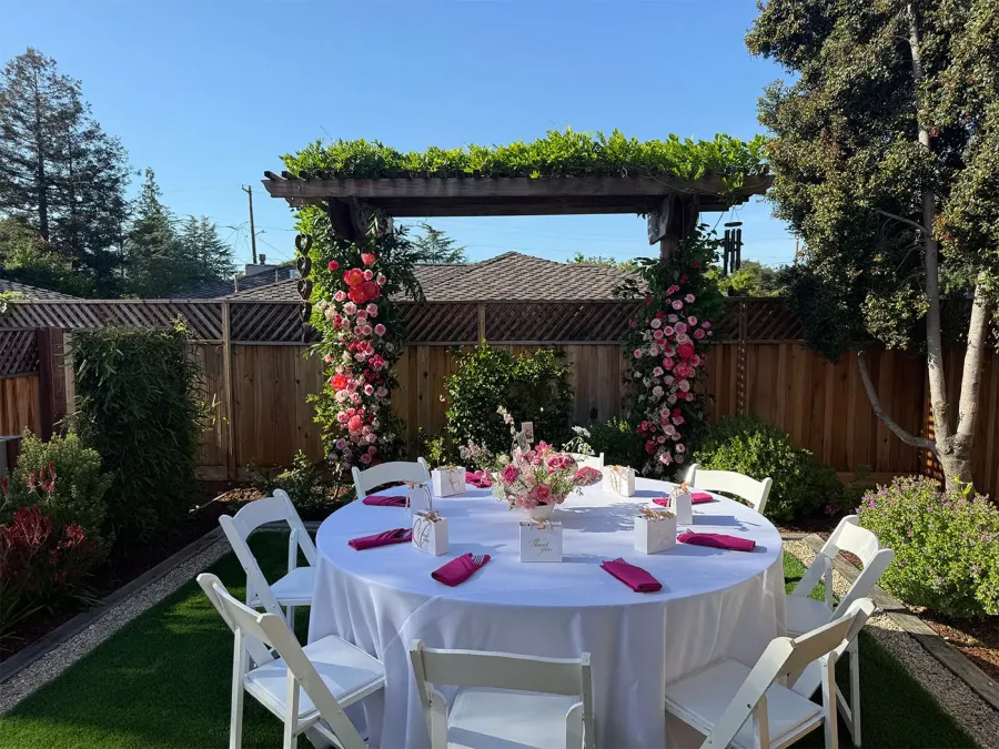 Rose arch in blush and deep red installed over a round garden table with white linen and fuchsia napkins — floral arch design for Walnut Creek catering weddings