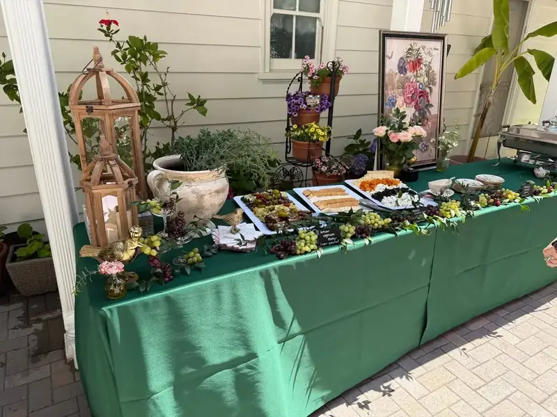Walnut Creek garden-party catering setup with cheeses, crackers, fruit, small bites, potted flowers, and an emerald tablecloth.